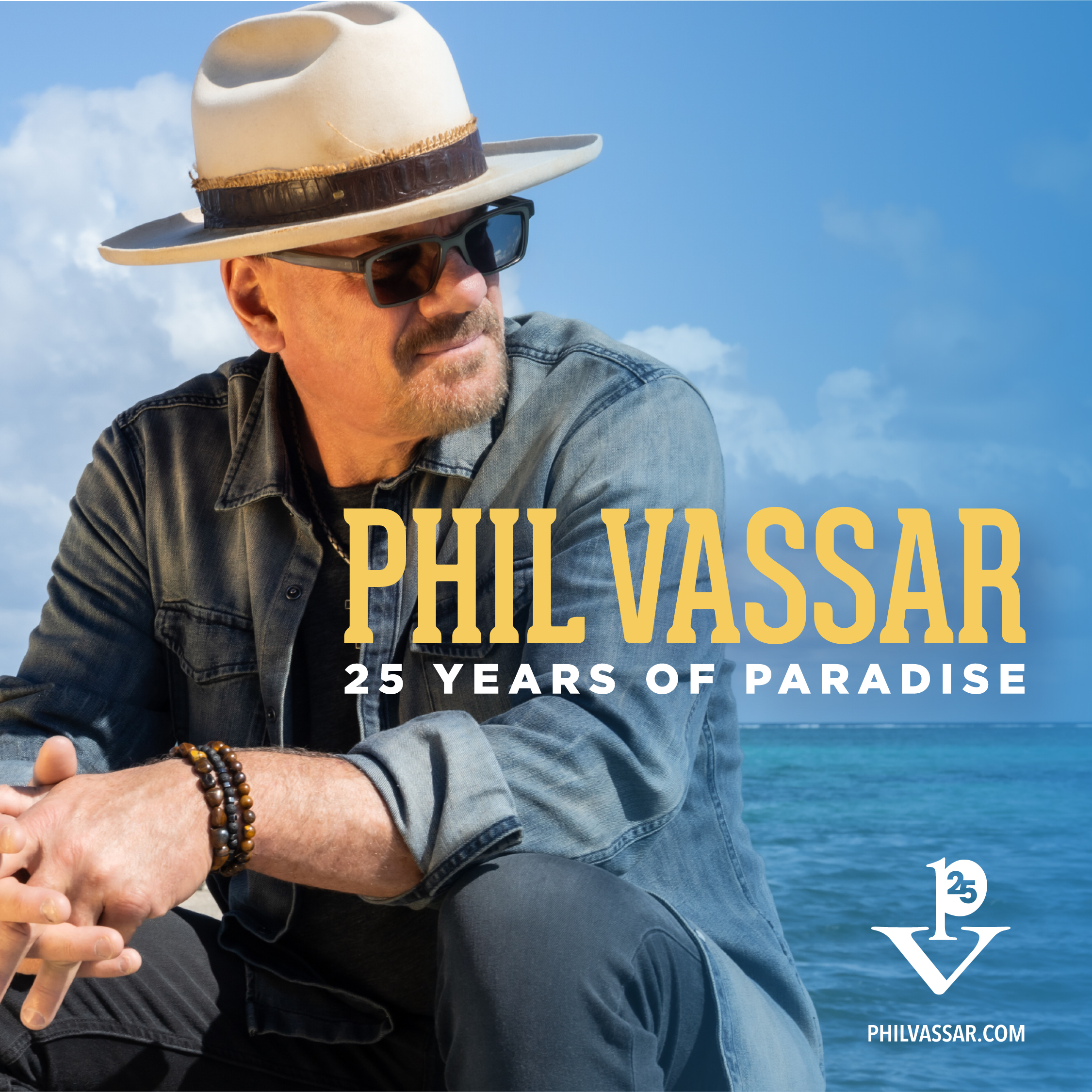A man in a hat and sunglasses sits by the ocean. Text reads PHIL VASSAR 25 Years of Paradise with a small anniversary logo and website in the corner.